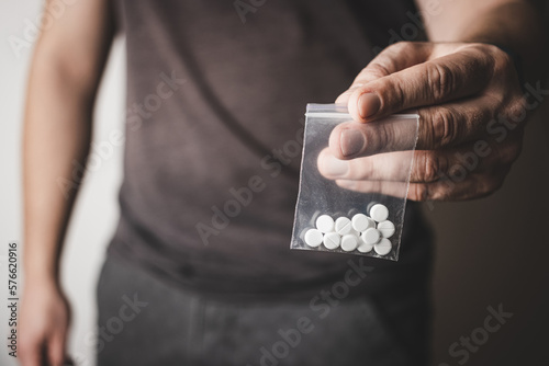 Man's hand holds transparent plastic packet with white pills lsd, drug dealer selling drugs. Drug abuse and addiction concept