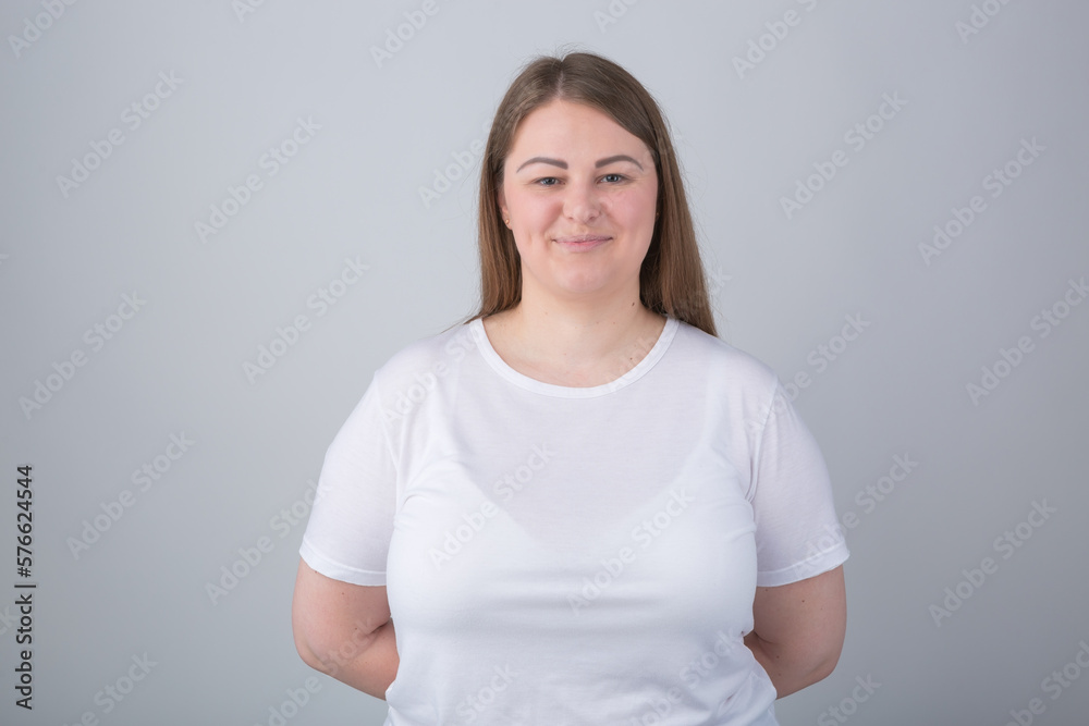 Cheerful plus size model posing in studio. Young Caucasian overweight woman wearing white t-shirt looking in camera with a smile