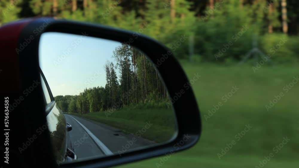 View in the rear view side mirror of a automobile, driving a red car along the road View in the rear view side mirror of a automobile, driving a red car along the road