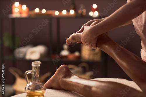 Closeup image of masseuse applying oil of feet of young woman