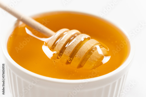Liquid natural bee honey in a white ceramic bowl with a wooden spoon.