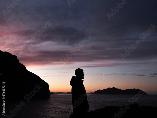 The man's silhouette with the sunset on the coast in the background.