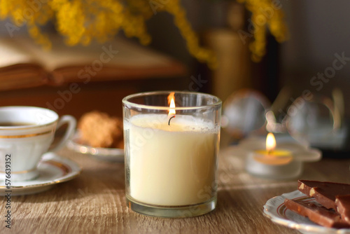 Scented candles, on the table. Selective focus.chocolate, cookies, cup of tea, books, e-reader, glasses and flowers on the table. Hygge at home. Selective focus.