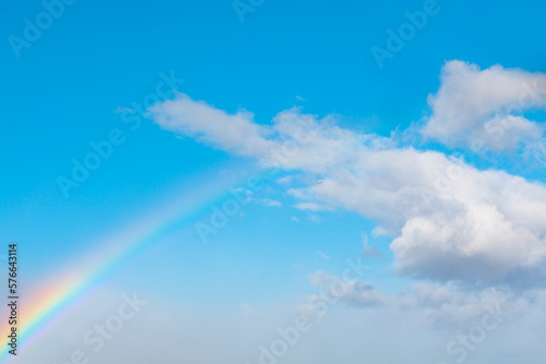 Rainbow and white clouds at blue sky . Celestial natural phenomenon