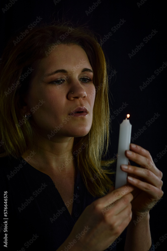 Obraz premium portrait of a beautiful blonde woman blowing out the flame of a candle she is holding