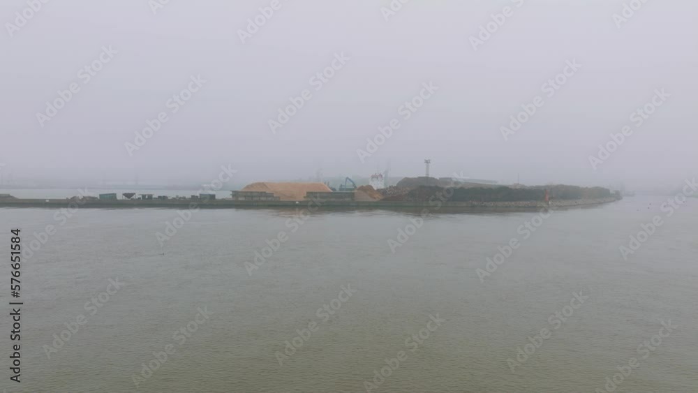 Aerial establishing view of wood terminal crane loading timber into the cargo ship, Port of Liepaja (Latvia), lumber log export, overcast day with fog and mist, wide drone drone shot moving forward Aerial establishing view of wood terminal crane loading timber into the cargo ship, Port of Liepaja (Latvia), lumber log export, overcast day with fog and mist, wide drone drone shot moving forward