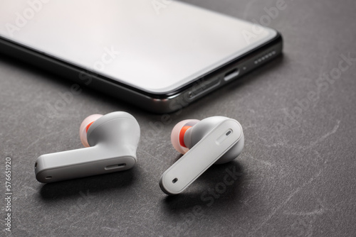 Wirelsss white headphones and smartphone on dark background