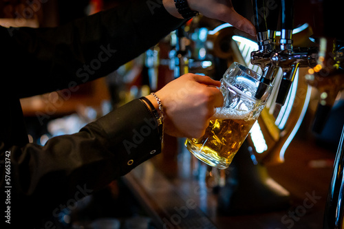 man bartender hand at beer tap pouring a draught beer in glass serving in a restaurant or pub