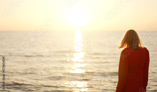 Woman in red dress looks at the sunset on the seashore. © M-Production