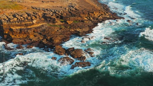 Ocean waves rolling to the rocky shore. Beautiful seascape. Aerial top view of the beautiful ocean rocky shore with rolling waves. Drone is hovering over rolling ocean waves to rocky shore