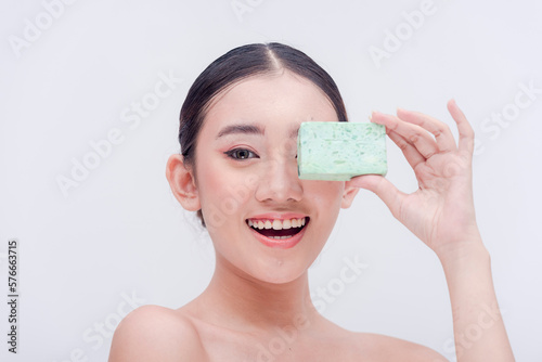 A smiling Southeast Asian millennial woman posing with a bar of exfoliating soap in her hand. Studio shot isolated on a plain white background. Beauty products and cosmetics endorser.