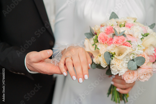 the groom holds the bride's hand with a bouquet and rings at the wedding