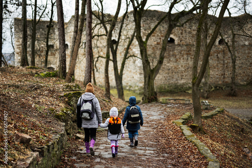 Back of mother and kids walk path to an ancient medieval fortress in rain. Terebovlia castle, Ukraine.