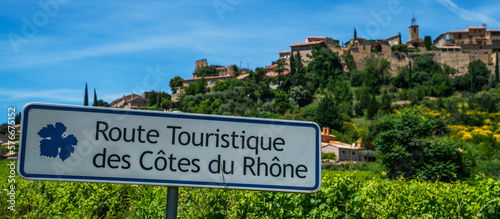 Road sign. Inscription in english "Tourist Route Cote du Rhone". Outside sign against blue sky, green vineyards and medieval town. Incredibly scenic drive through the southern Cotes-du-Rhone Villages.