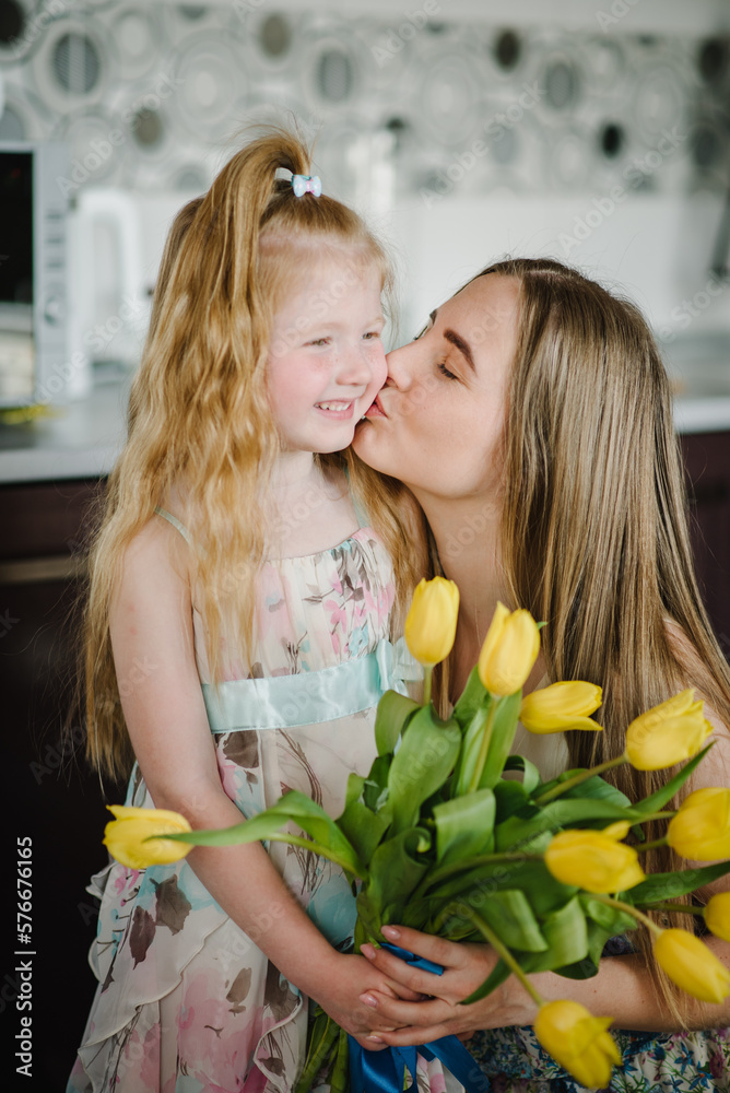 Daughter congratulates mother and gives bouquet of yellow tulip flowers in kitchen at home. Mother's day concept. Mom and child girl hug and kiss. Greeting card for International Women's Day. Closeup. Daughter congratulates mother and gives bouquet of yellow tulip flowers in kitchen at home. Mother's day concept. Mom and child girl hug and kiss. Greeting card for International Women's Day. Closeup.