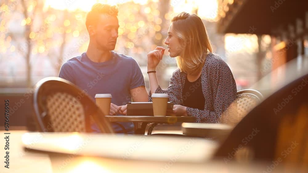 Happy young couple having a coffee together and looking at a digital tablet