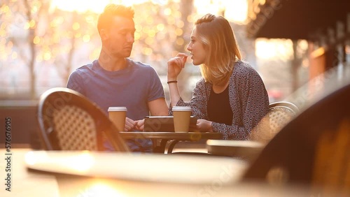 Happy young couple having a coffee together and looking at a digital tablet