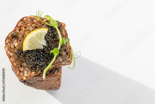 Obraz na płótnie Black caviar on a sandwich with eggs, lemon, greenery w salonie