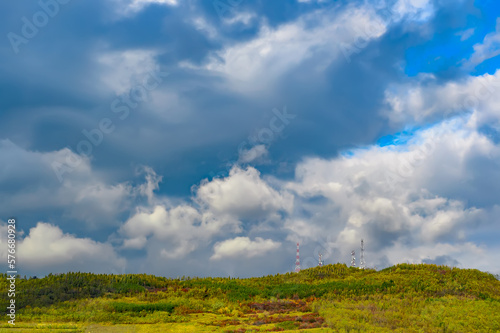 Towers with telecommunication antennas located on top of the hills covered in colorful trees, autumn dramatic landscape with stormy clouds rushing over the dark blue sky. Natural vibrant Earth scenery