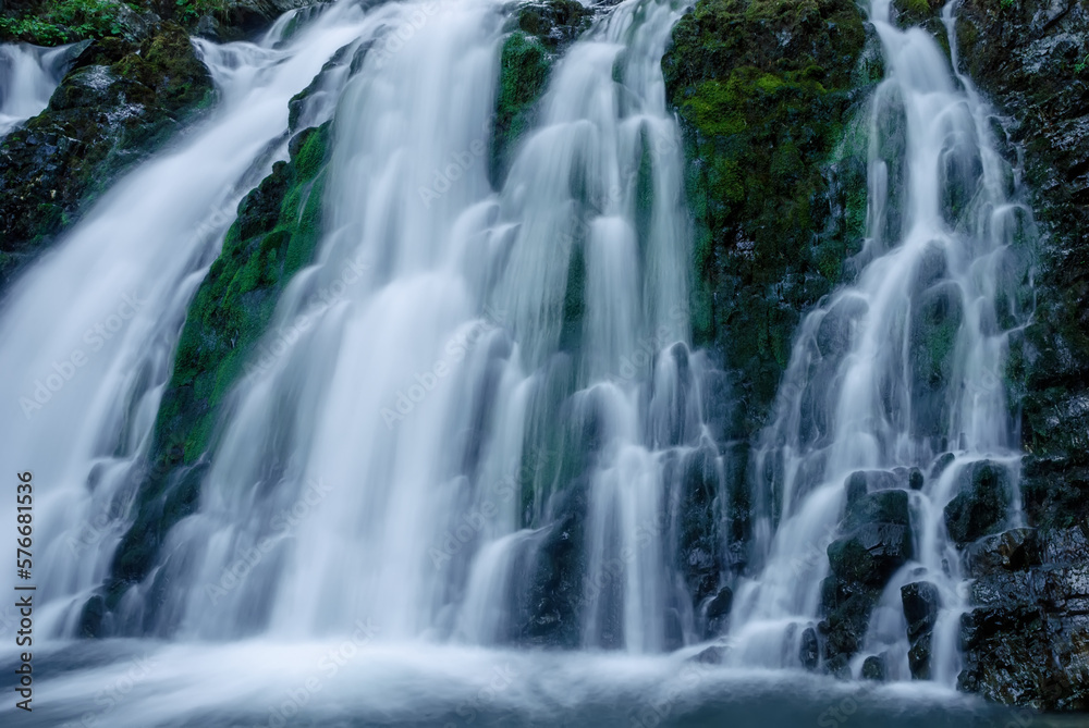 Beautiful mountain rainforest waterfall with fast flowing water and rocks, long exposure. Natural seasonal travel outdoor background with sun shining. Stream waterfall on rocks in the forest