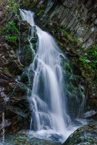 Beautiful mountain rainforest waterfall with fast flowing water and rocks, long exposure. Natural seasonal travel outdoor background with sun shining. Stream waterfall on rocks in the forest