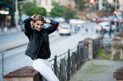 Smiling woman in the city street wearing black leather jacket and white pants and sunglasses