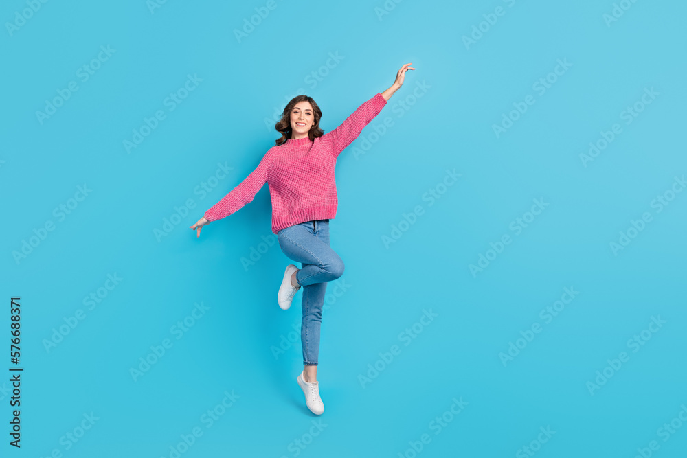 Full length photo of young careless relaxed girl model wear pink knitwear new denim jeans flying wings hands isolated on blue color background Full length photo of young careless relaxed girl model wear pink knitwear new denim jeans flying wings hands isolated on blue color background