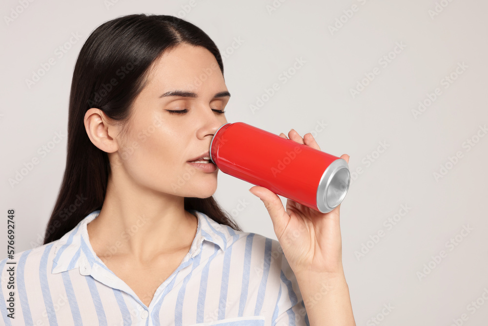 Beautiful young woman drinking from tin can on light grey background Beautiful young woman drinking from tin can on light grey background
