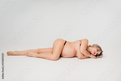 a naked pregnant against the background of a white cyclorama in a photo studio. 
