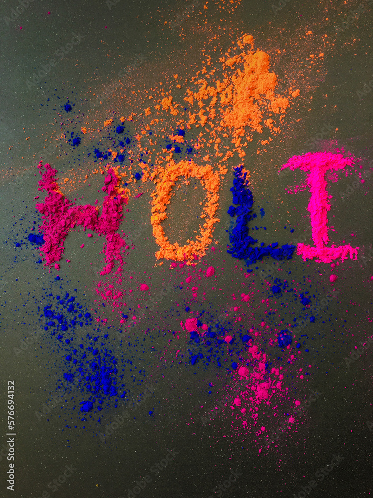 'Holi' word written by powder colors on dark background. Holi - an Indian festival of colors celebration message.