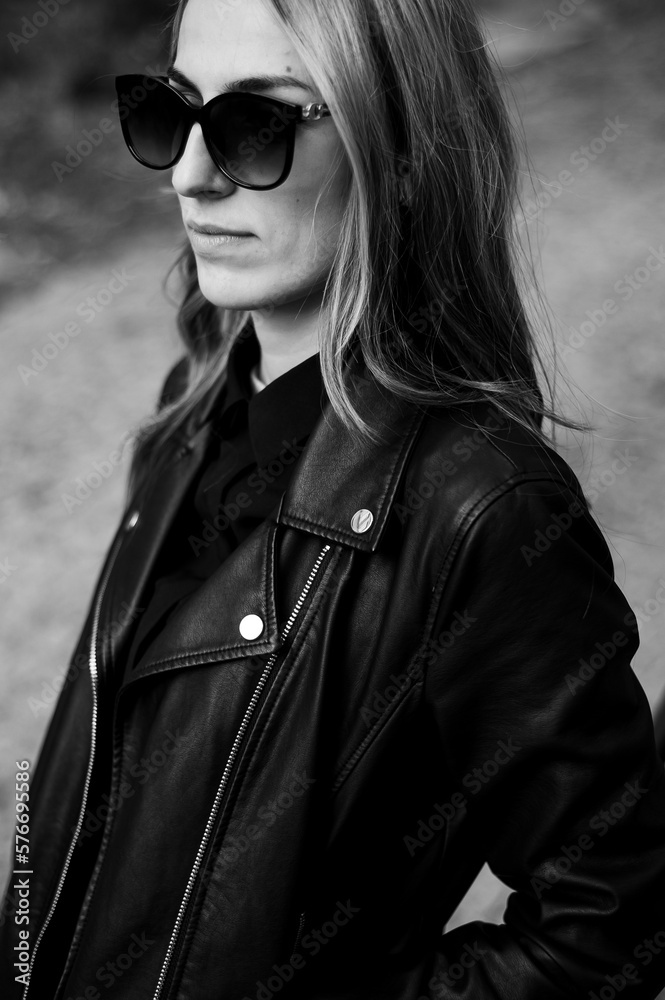 A woman wearing a black leather jacket and sunglasses smiles. A woman wearing a black leather jacket and sunglasses smiles.