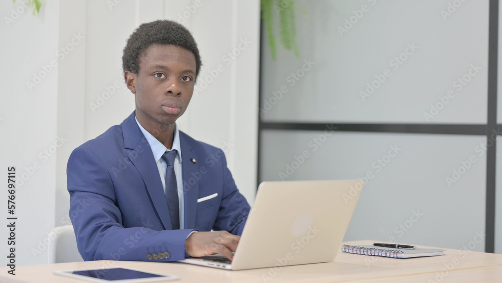 African Businessman Looking at Camera while using Laptop African Businessman Looking at Camera while using Laptop