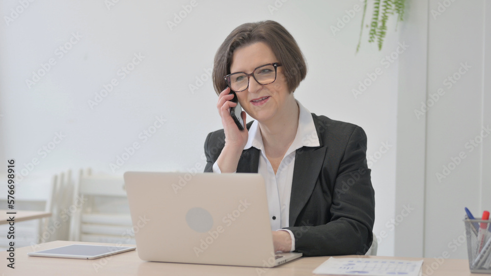 Old Businesswoman Talking on Phone while using Laptop Old Businesswoman Talking on Phone while using Laptop