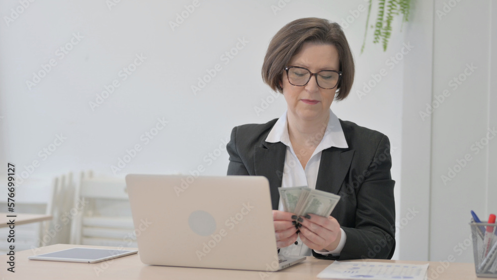 Old Businesswoman Counting Dollar while Working on Laptop Old Businesswoman Counting Dollar while Working on Laptop
