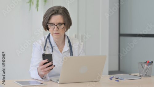 Old Female Doctor using Smartphone while using Laptop