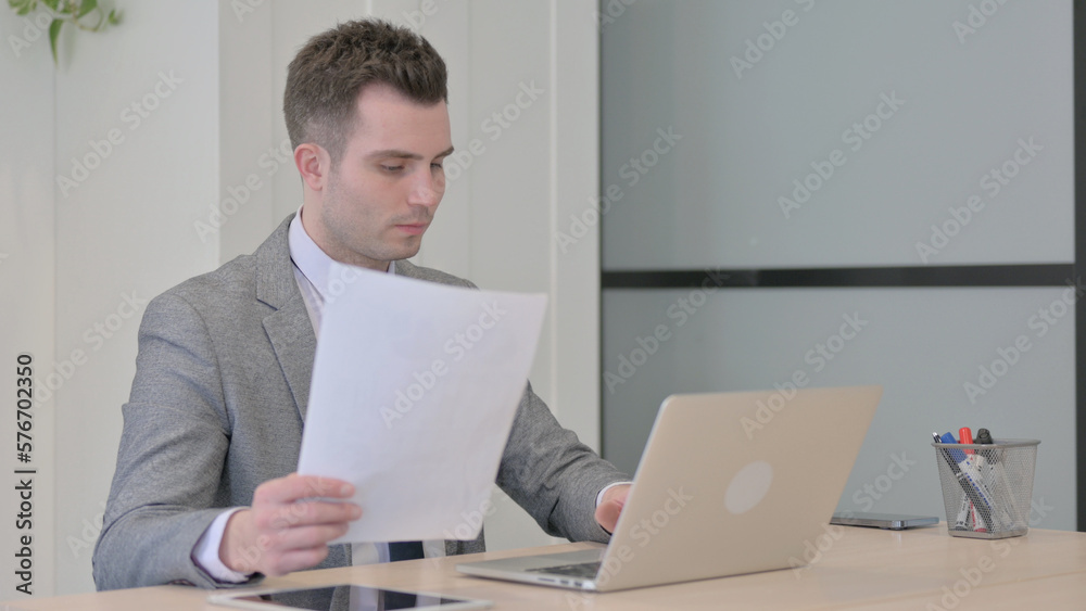 Obraz premium Young Businessman Working on Laptop and Documents