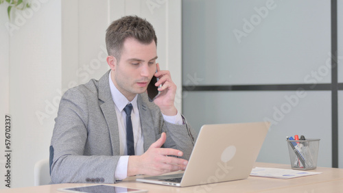 Young Businessman Talking on Phone while using Laptop