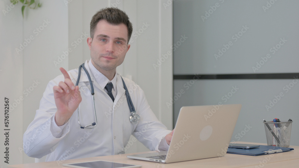 Young Doctor Shaking Head and Finger in Rejection while Working on Laptop Young Doctor Shaking Head and Finger in Rejection while Working on Laptop