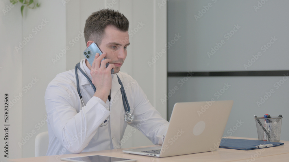 Young Doctor Talking on Phone while using Laptop Young Doctor Talking on Phone while using Laptop