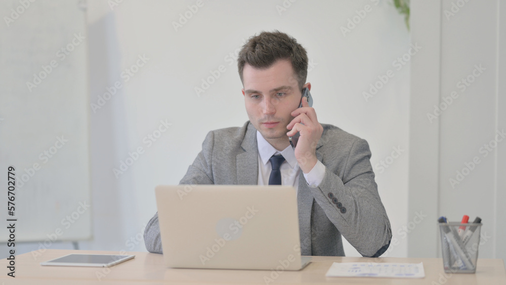 Young Businessman Talking on Phone while using Laptop Young Businessman Talking on Phone while using Laptop