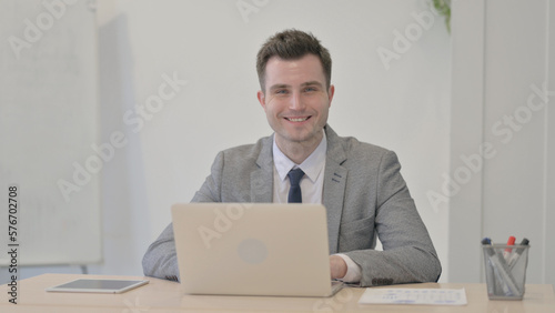 Young Businessman Smiling at Camera while using Laptop