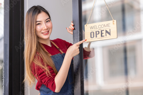 Asian woman is a waitress in an apron, the owner of the cafe stands at the door with a sign Open waiting for customers. SME Small business concept, cafes and restaurants 
