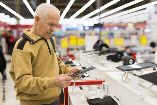 Obraz na plátně elderly grayhaired man pensioner examining counter with electronic gadgets and t