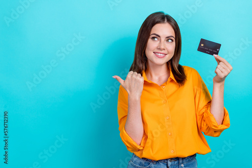 Portrait of positive girl with bob hairstyle dressed yellow shirt hold card directing look empty space isolated on blue color background