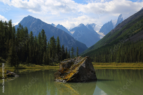 Picturesque landscape with mountains and a greater stone in middle of a green smooth surface of water