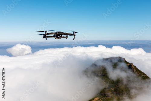 Drone with camera flying over the mountain peak and white clouds.