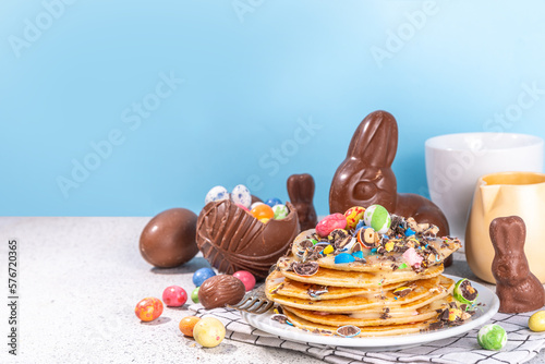 Children's funny cute breakfast for Easter. American pancakes, fried batter cakes with Easter chocolate eggs, marshmallows, sugar topping with broken chocolate eggs sprinkle decor