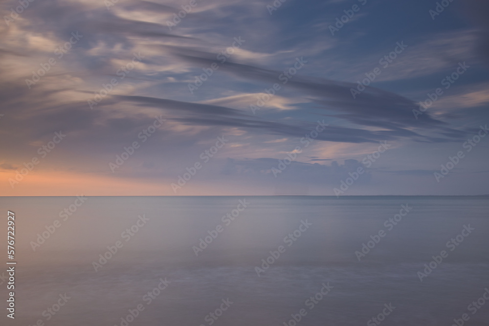 Horizontal view on the sea with calm water. North sea during sunset with dramatic dark clouds at the sky. Seascape with copy space and long exposure