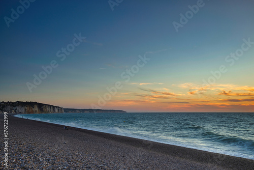 Horizontal view of the rocky coast, gravel beach and North sea water in Normandy France during sunset with clouds at the sky. Seascape with copy space