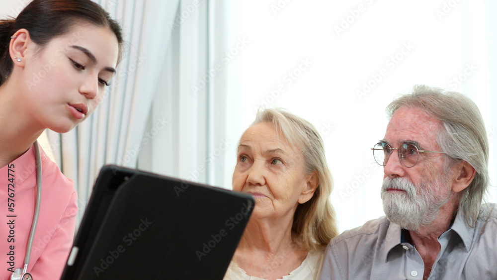 Obraz premium Caucasian young adult nurse is visiting elderly couple and holding a tablet to show medical records. Female caregiver is explaining result of medical examination and treatment to senior grandparents.&nbsp;